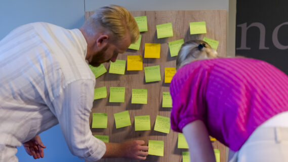 Deelnemers plakken post it op een muur tijdens een workshop