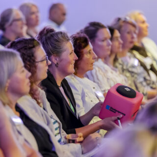 Een deelnemer in de zaal heeft een catchbox met een microfoon erin om een centrale vraag te stellen