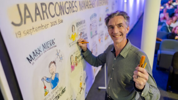 Een tekenkunstenaar poseert voor de camera, voor het doek waar die de hele dag heeft getekend